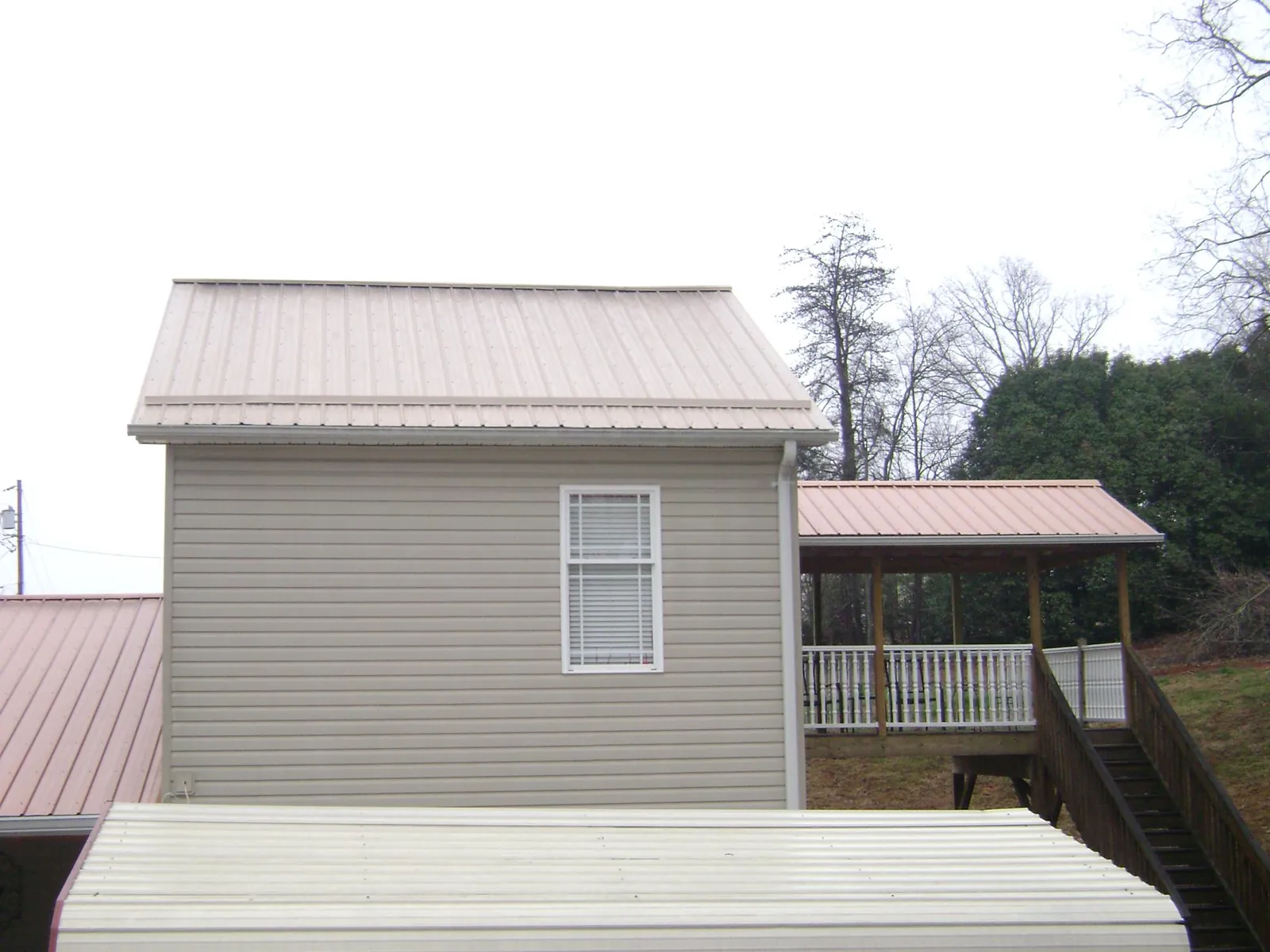 Tan metal roofs on a two story addition and attached porch, from a Roof Replacement job in Blissfield